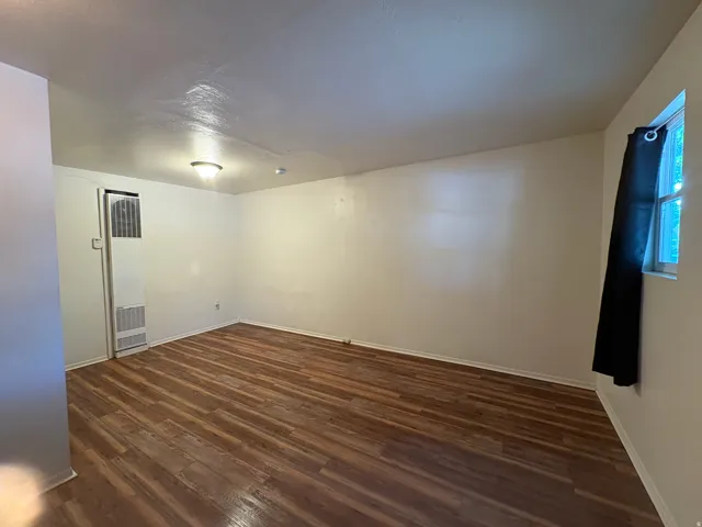 Spacious room featuring wood-finish flooring, white painted walls, and a window with natural light