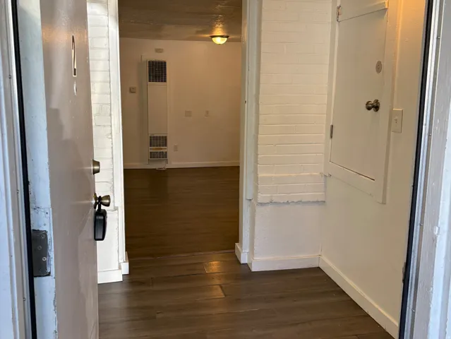 Entryway featuring wood-finish flooring, white painted brick walls, and a wall-mounted light fixture