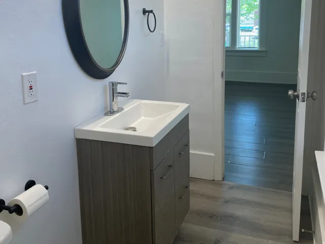 Bathroom featuring a wood-finish vanity with an integrated sink, polished chrome faucet, and a wall-mounted oval mirror