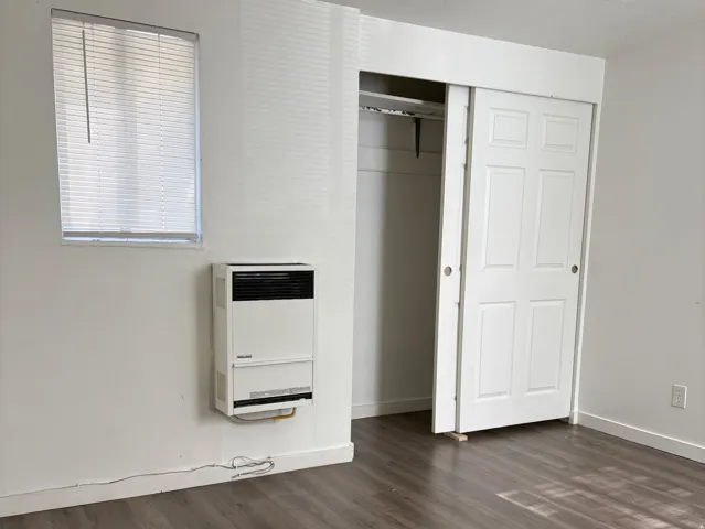 Interior space featuring wood-finish flooring, white walls, and a built-in wall heater