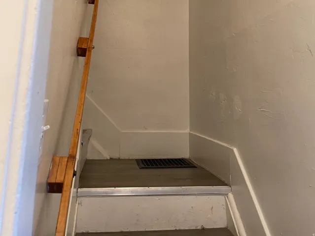 Stairwell featuring a wood handrail, painted walls, white trim, and a floor vent