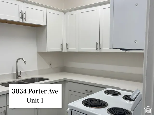 Modern kitchen featuring white shaker cabinetry, stainless steel hardware, a double basin sink with a gooseneck faucet, light-toned countertops, and a white electric range