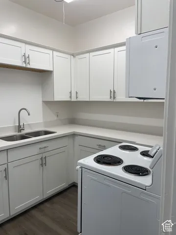 Modern kitchen featuring white shaker cabinetry, light-toned countertops, a double basin sink with a gooseneck faucet, a white electric range, and wood-finish flooring