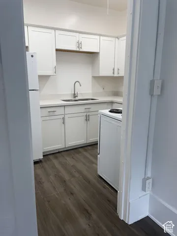 Kitchen featuring white cabinetry, light countertops, a stainless steel sink with a gooseneck faucet, a white refrigerator, and wood-finish flooring