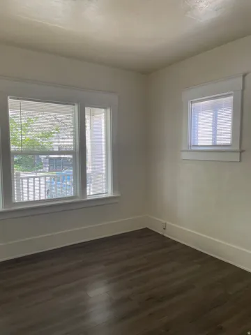Room featuring wood-finish flooring, two windows with blinds, and white trim