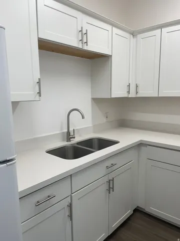 Kitchen featuring white shaker-style cabinetry, light-toned countertops, a stainless steel double-basin sink, and a high-arc faucet
