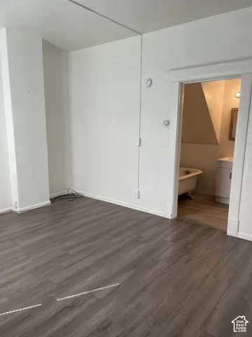Spacious interior room featuring wood-finish flooring, white baseboards, and a doorway opening to a bathroom with a clawfoot tub and tile wainscoting