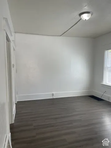 Spacious interior room featuring wood-finish flooring, white baseboards, and a white ceiling with a flush-mount light fixture