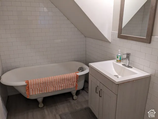 Bathroom featuring a clawfoot tub, white subway tile surround, wood-finish flooring, and a vanity with an integrated sink and chrome faucet