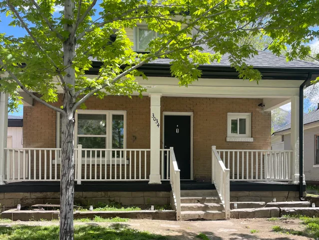 Brick facade residence featuring a covered front porch with white railings, concrete steps, and a dark entry door