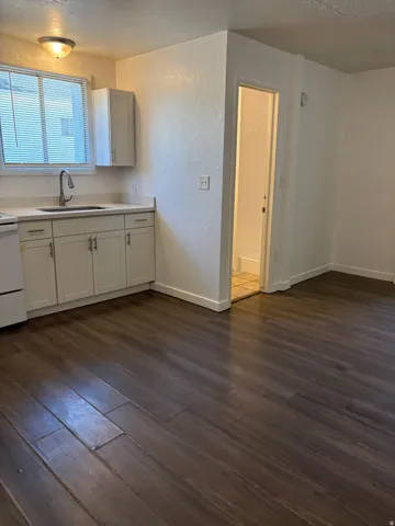 Kitchen area featuring dark wood-finish flooring, white cabinetry, light-toned countertops, and a stainless steel gooseneck faucet