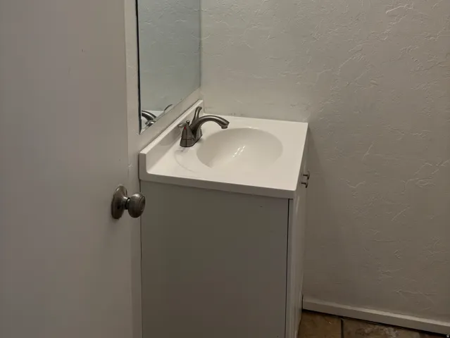 Single vanity with an integrated white sink and brushed nickel faucet, a rectangular mirror, and a three-bulb vanity light fixture