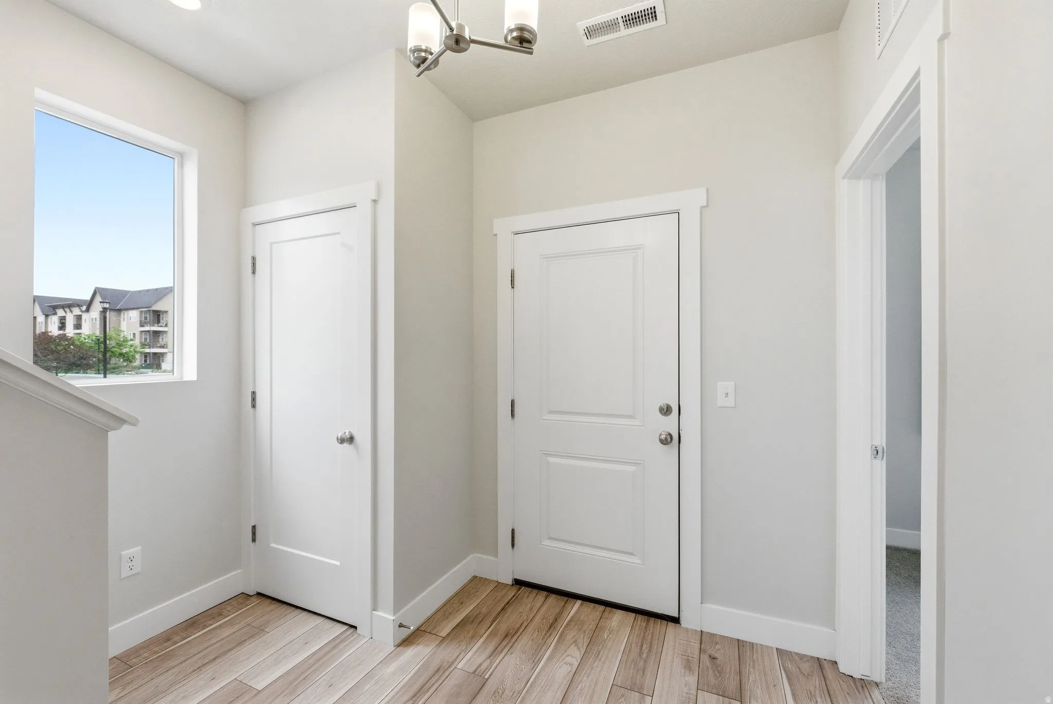 Entryway featuring wood-finish flooring, a contemporary chandelier, white trim, and light gray wall paint
