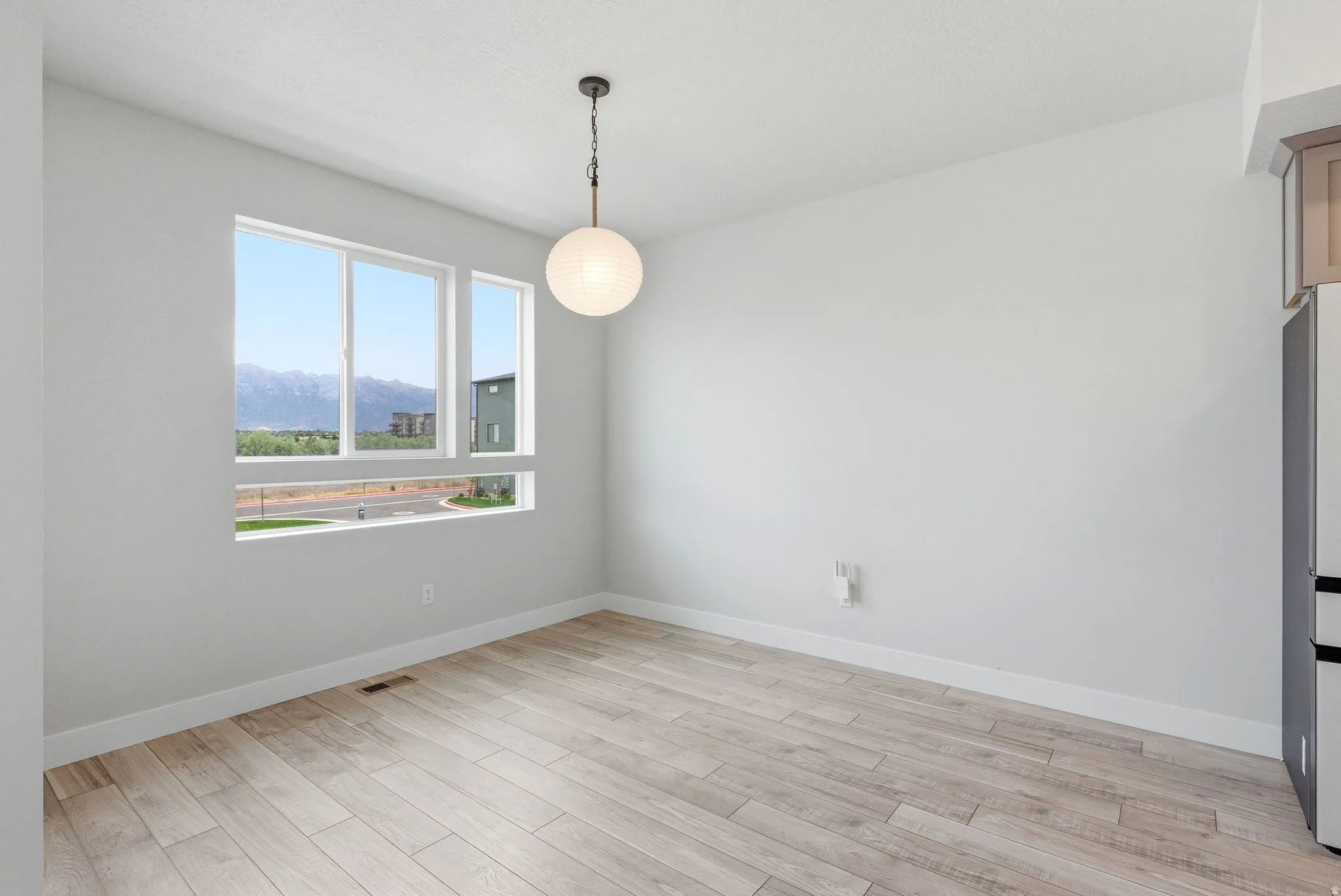 Spacious room featuring multiple white-framed windows, a modern spherical pendant light, and wood-finish flooring