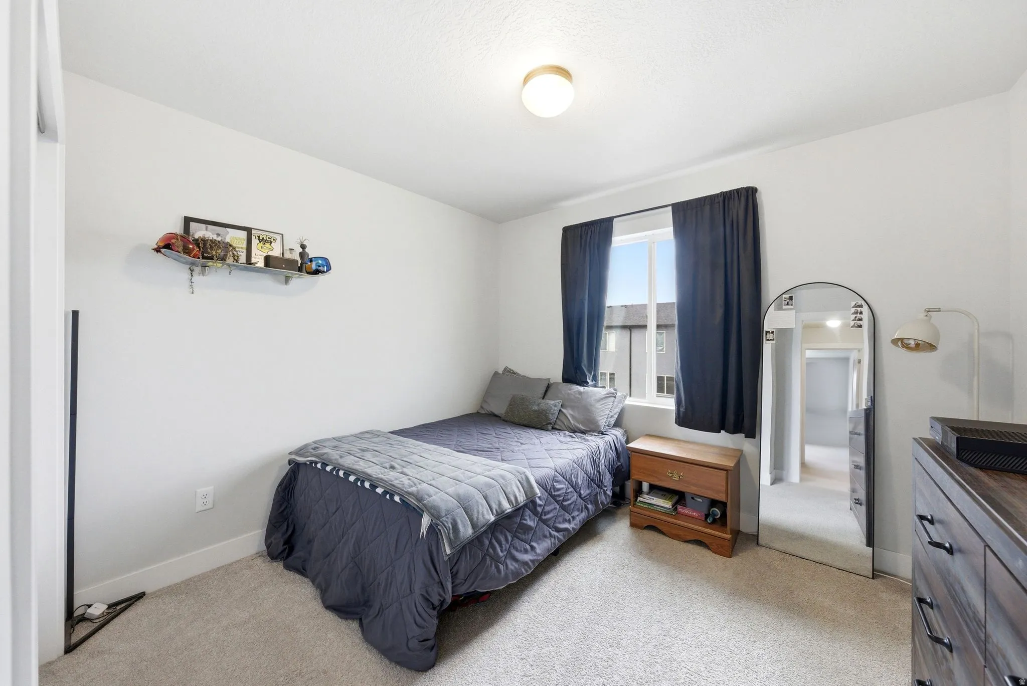 Bedroom with light-colored carpeting, a window featuring dark curtains, and white painted walls