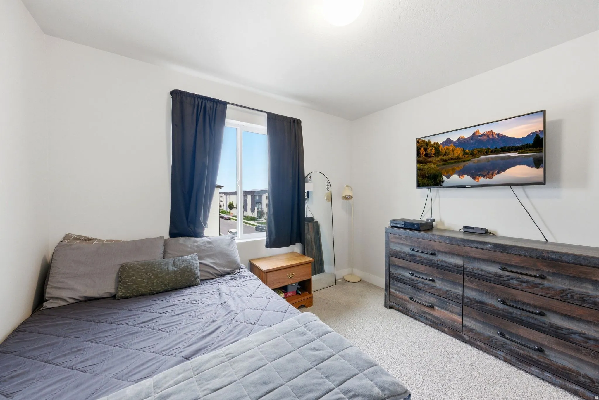 Bedroom featuring light-toned carpeting and a window with dark drapery