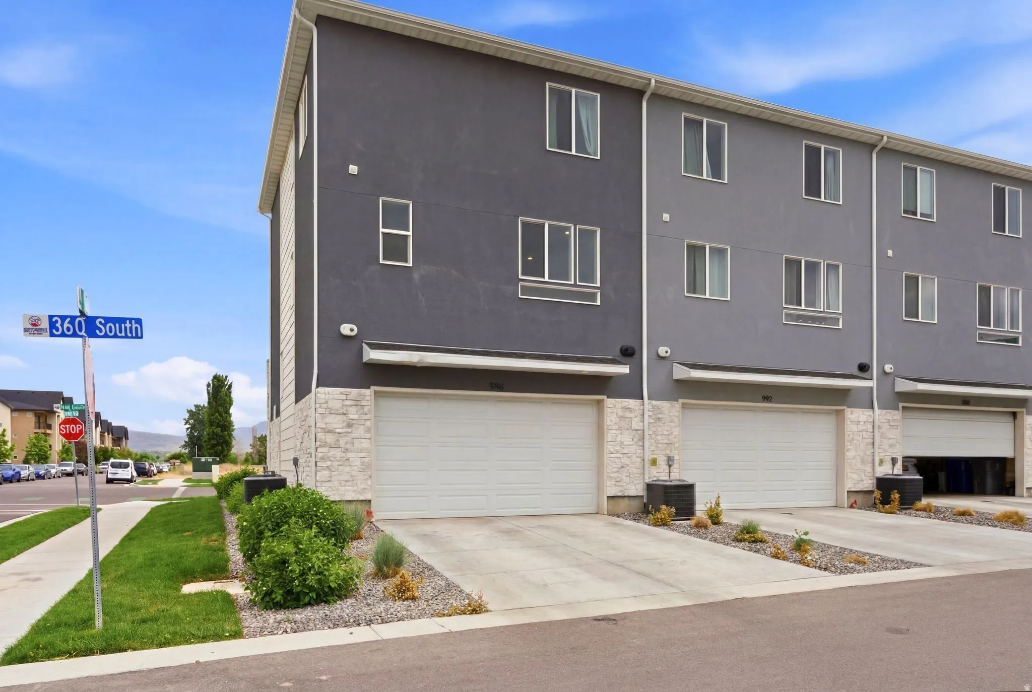 Multi-story townhome featuring a dark gray stucco facade and stone veneer accents