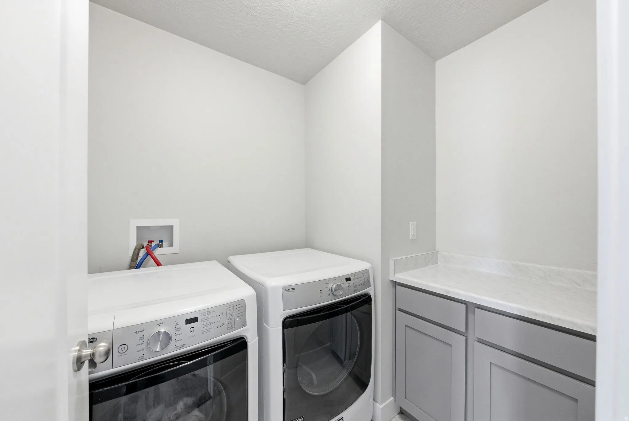 Dedicated laundry space featuring a side-by-side washer and dryer, light gray cabinetry, and a light-toned countertop