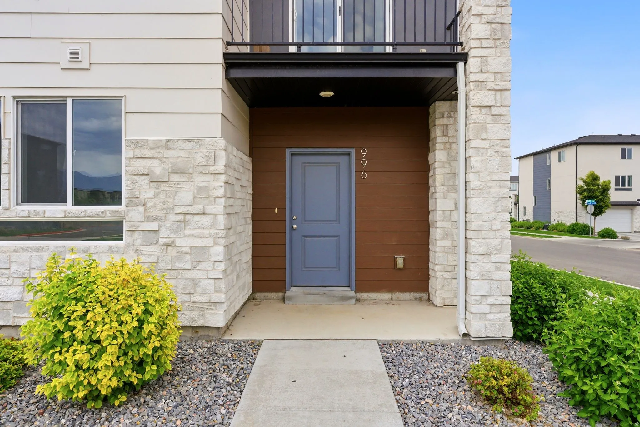 Modern exterior showcasing an entry door with metal house numbers, horizontal wood-finish siding, and light-toned stacked stone accents