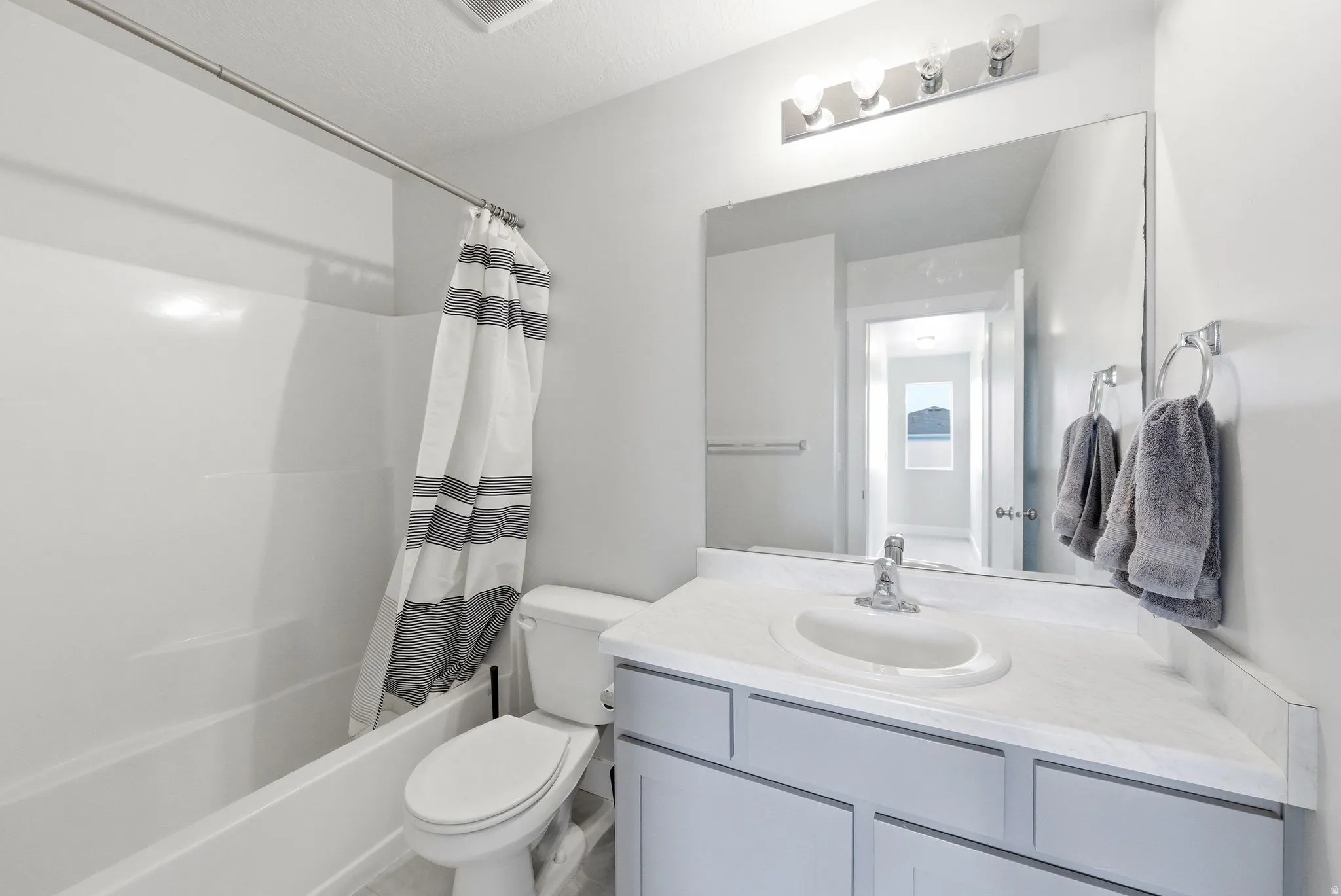 Full bathroom featuring a white tub and shower combination with a single-handle faucet, a vanity with a white countertop and integrated sink, a large mirror, and a three-bulb vanity light fixture