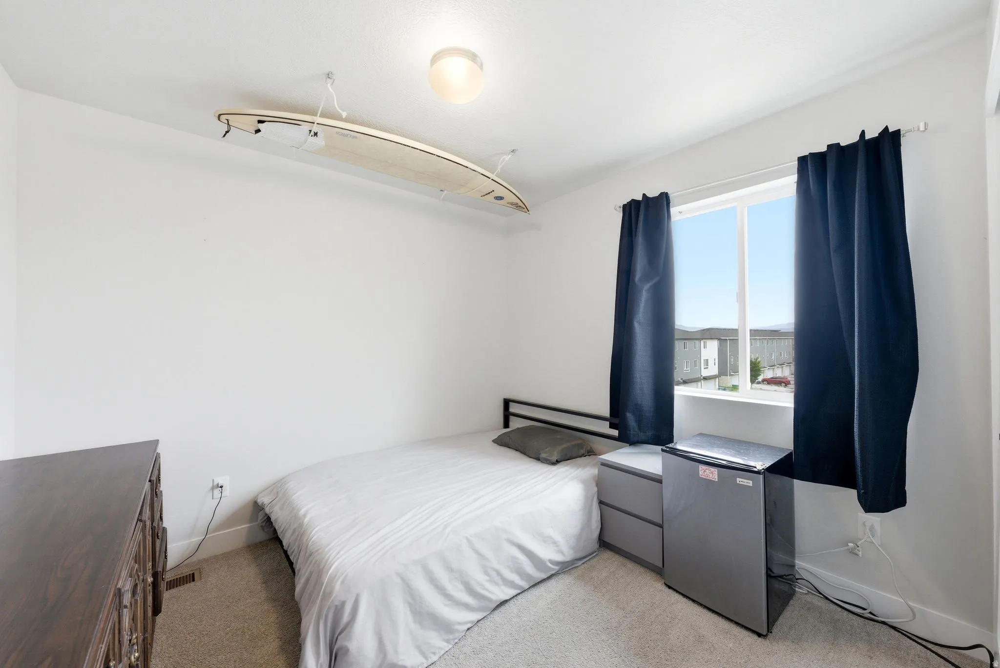 Bright room featuring a window with dark curtains, light-colored walls, and neutral carpet