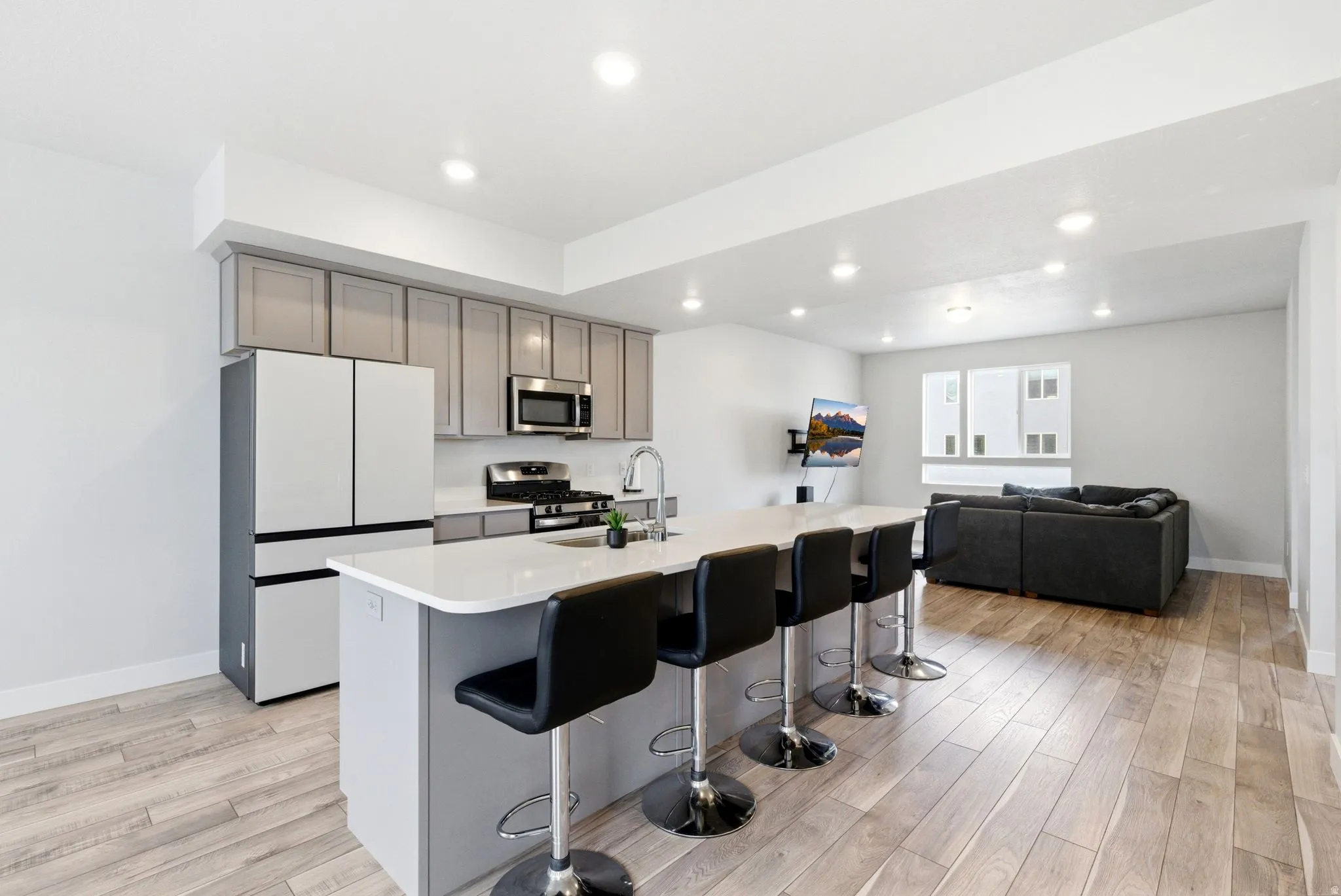 Open-concept kitchen featuring an island with a light-colored countertop, light gray cabinetry, stainless steel appliances, and wood-finish flooring