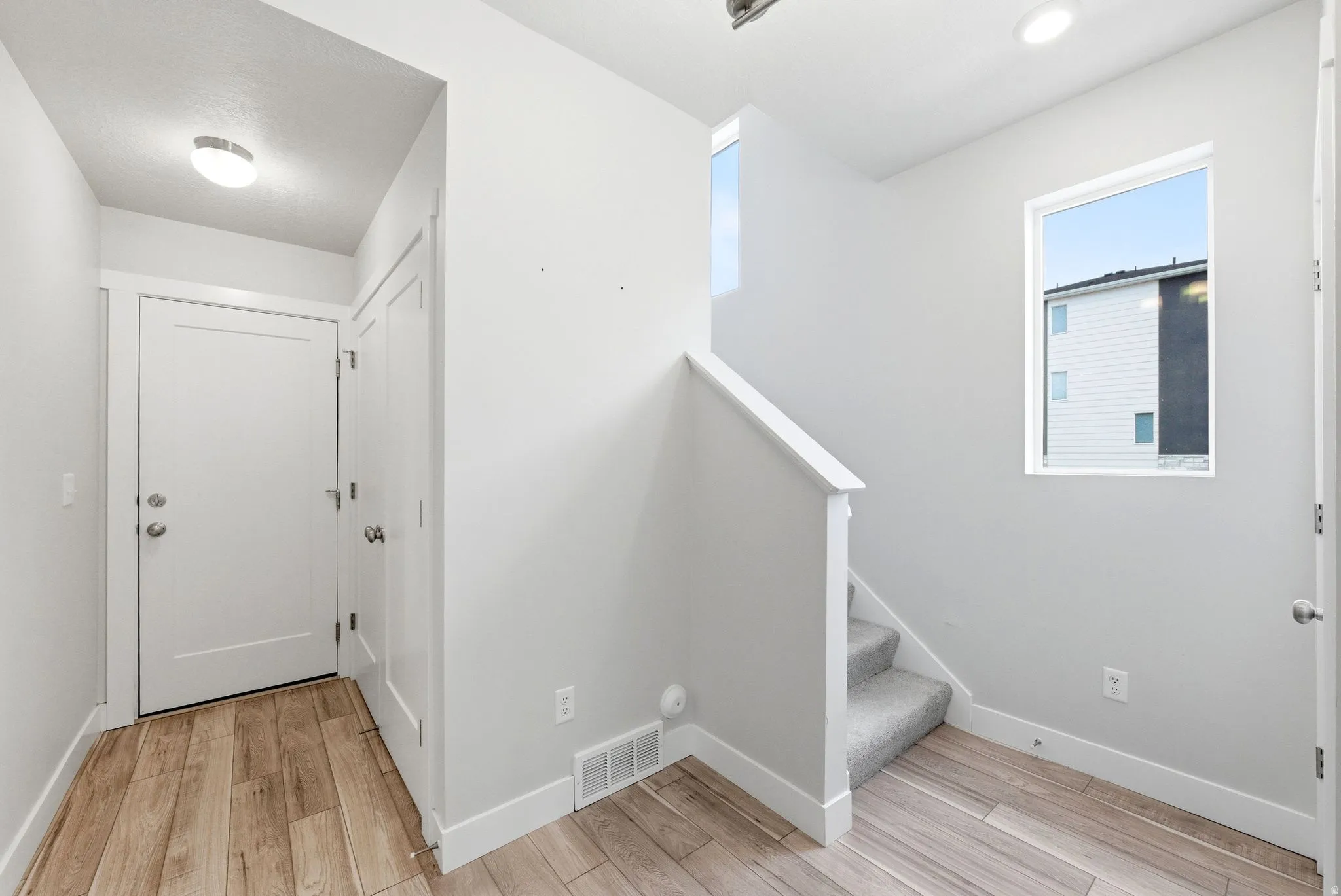 Entryway featuring wood-finish flooring, white walls, and a staircase with carpeted treads