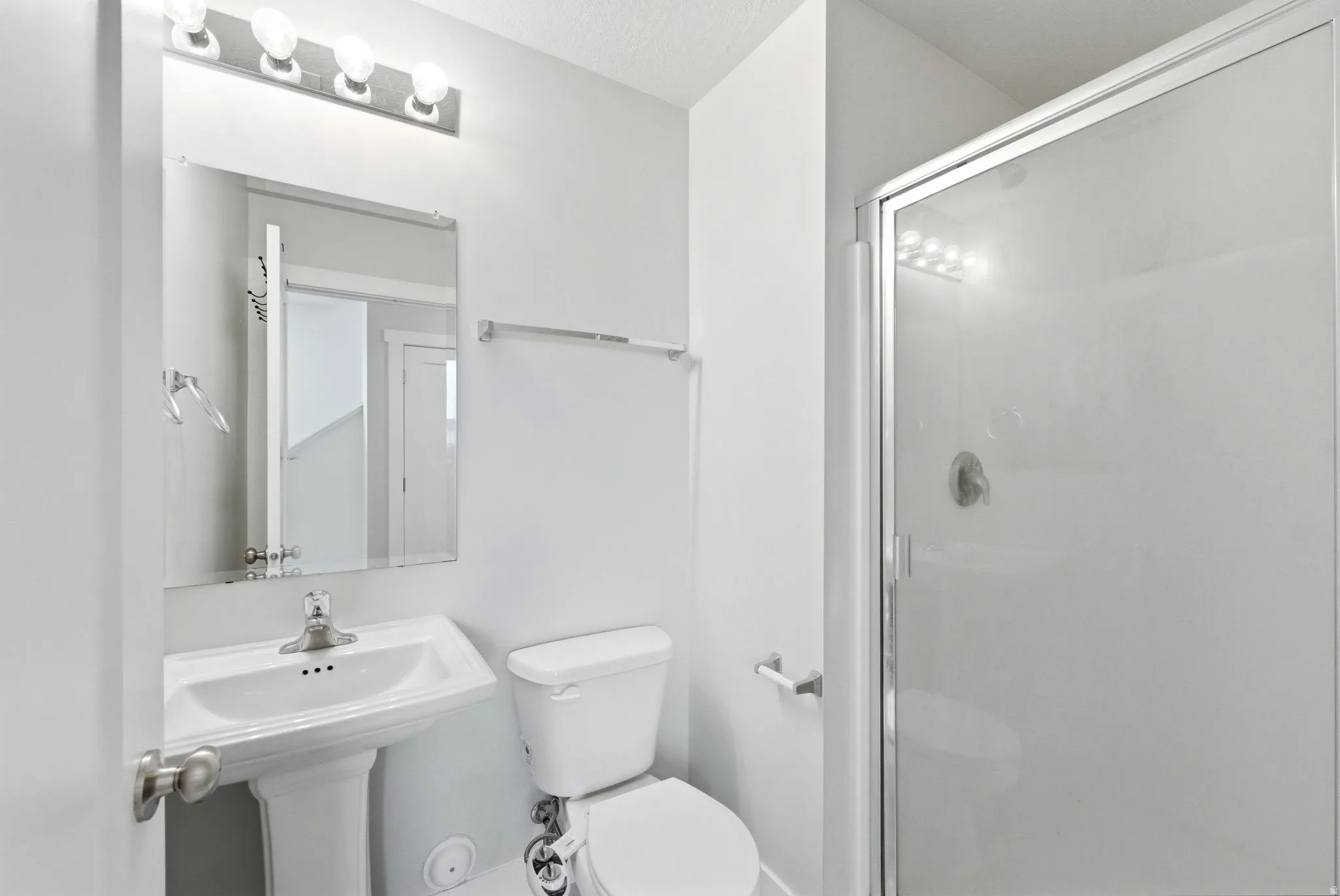 Bathroom featuring a glass-enclosed shower, pedestal sink with chrome faucet, wall-mounted mirror, and vanity lighting
