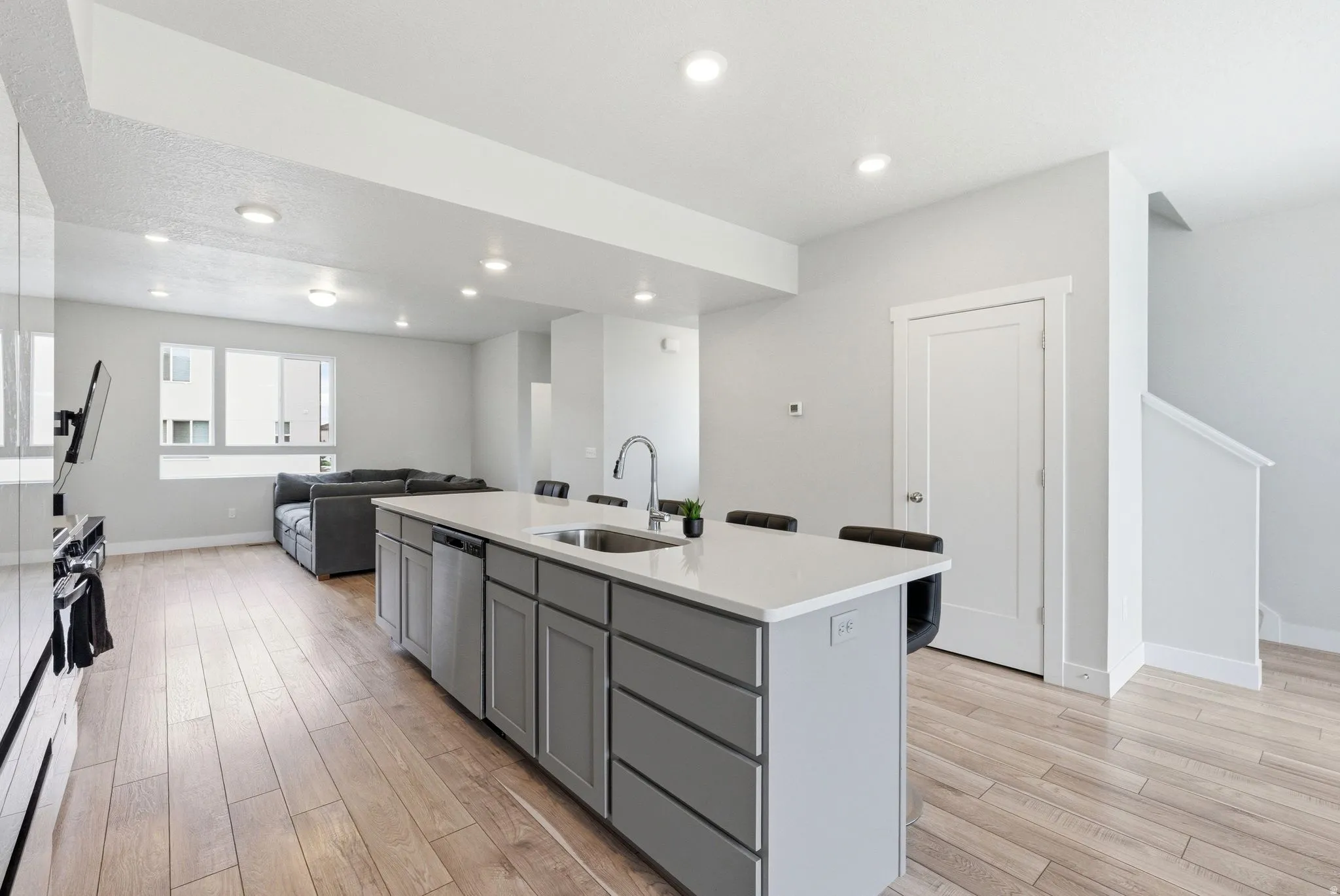 Kitchen island featuring a stainless steel sink with a high-arc faucet, light-toned countertop, and grey cabinetry