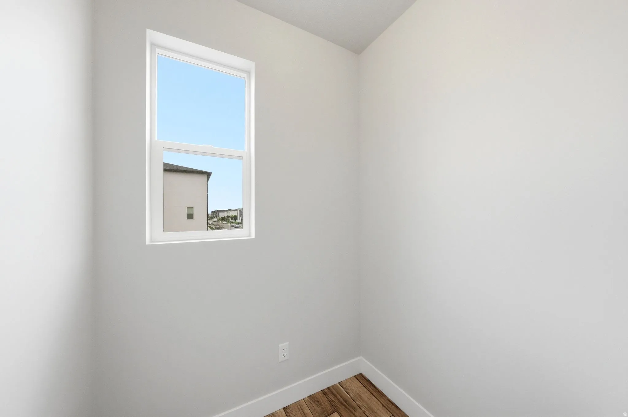 Neutral tone wall finish with a double-hung window, white trim, and wood-finish flooring