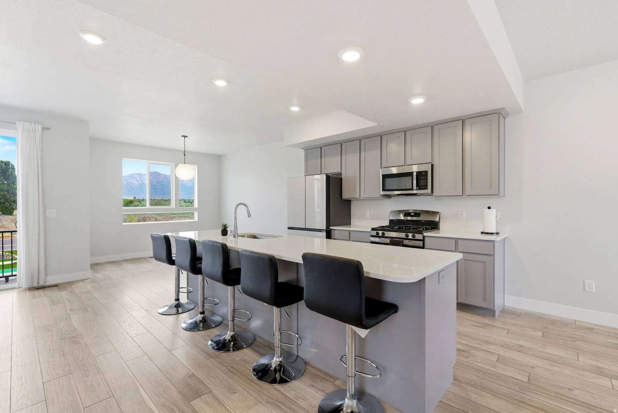 Bright kitchen featuring a large central island with seating, light gray cabinetry, stainless steel appliances, and light wood-finish flooring