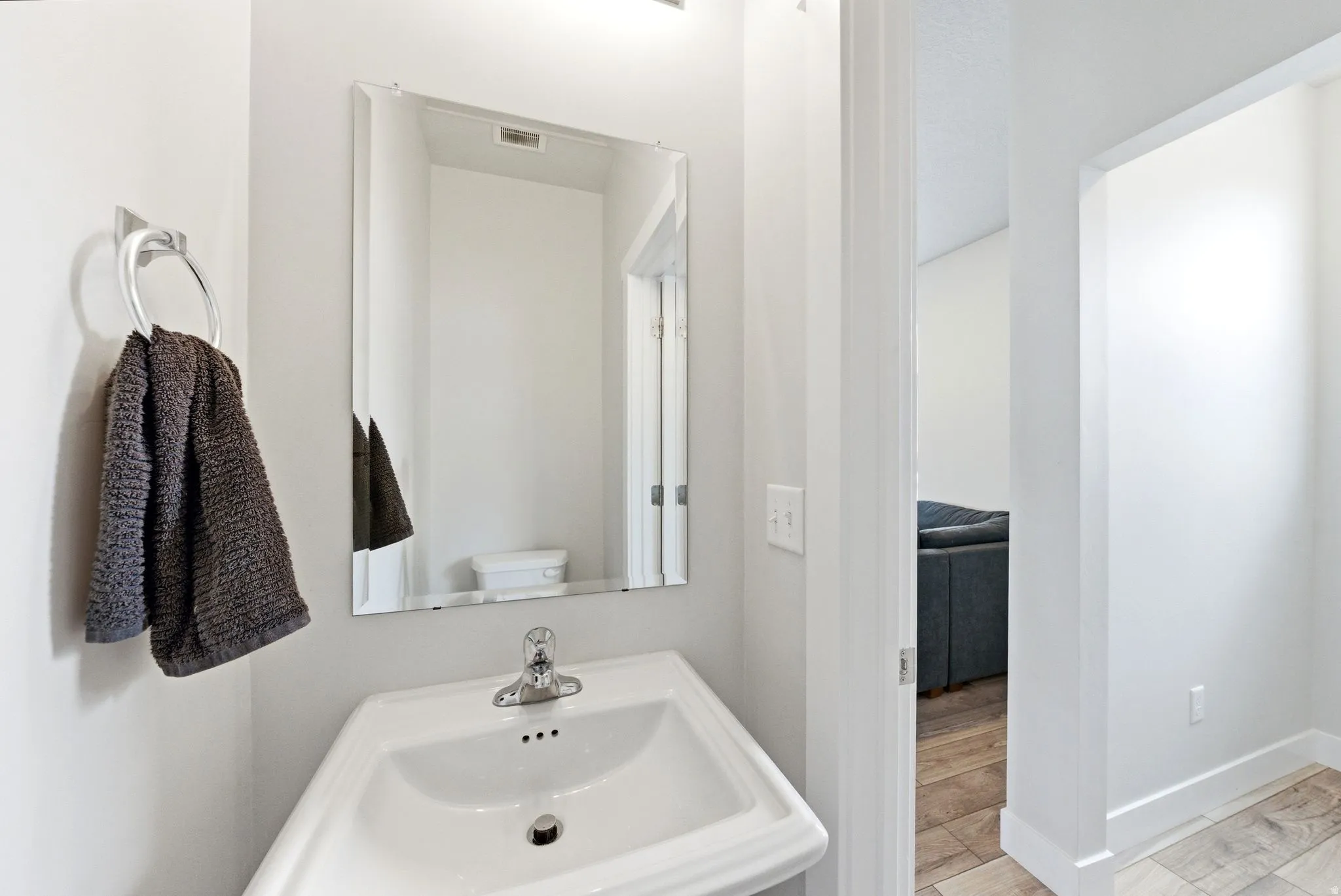 Pedestal sink with chrome faucet, complemented by a rectangular frameless mirror and overhead lighting