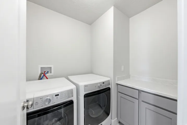 Dedicated laundry space featuring a side-by-side washer and dryer, light gray cabinetry, and a light-toned countertop