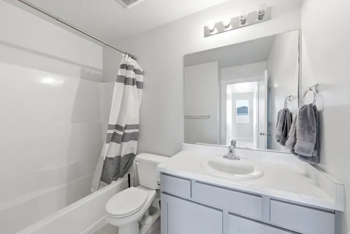 Full bathroom featuring a white tub and shower combination with a single-handle faucet, a vanity with a white countertop and integrated sink, a large mirror, and a three-bulb vanity light fixture