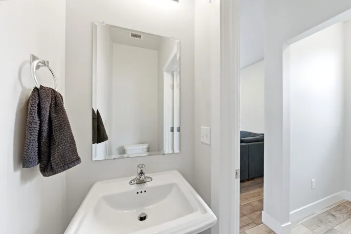 Pedestal sink with chrome faucet, complemented by a rectangular frameless mirror and overhead lighting