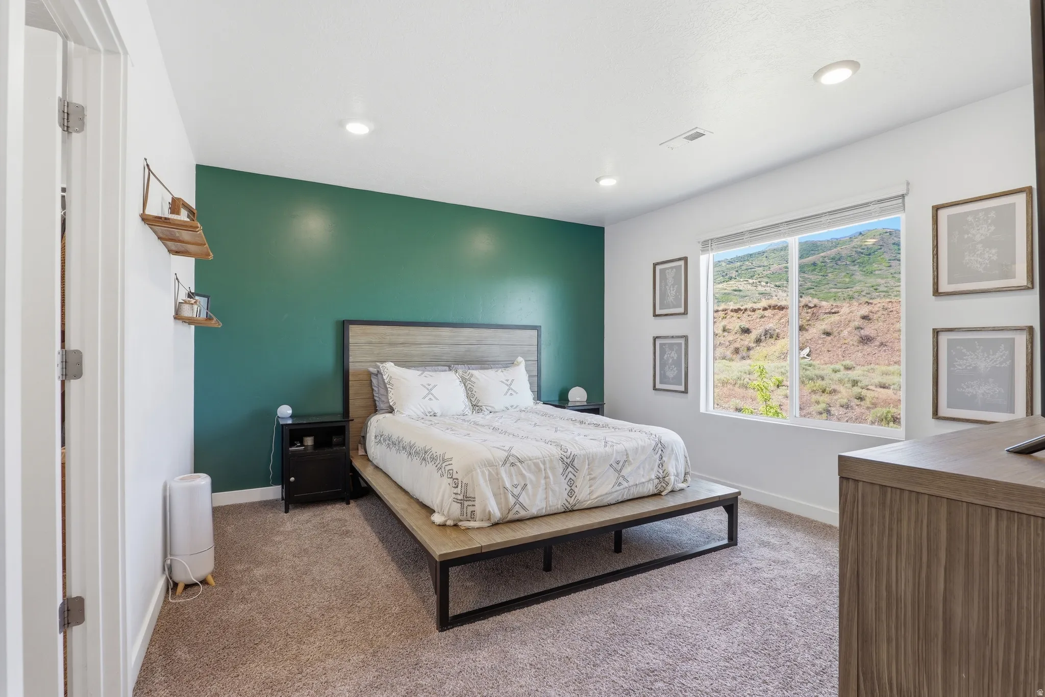 Carpeted room featuring a large window with roller shades, a green accent wall, recessed lighting, and a view of natural terrain