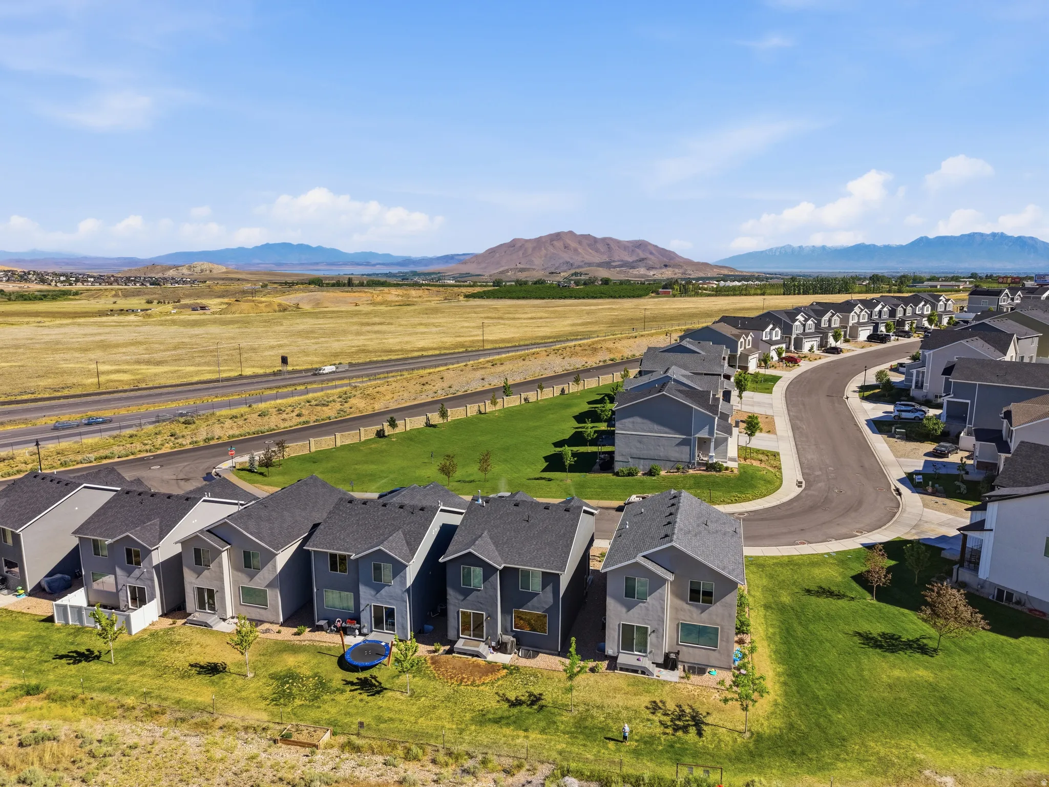 Contemporary residential development featuring a curving street, individual plots with manicured lawns, and a distant mountain backdrop