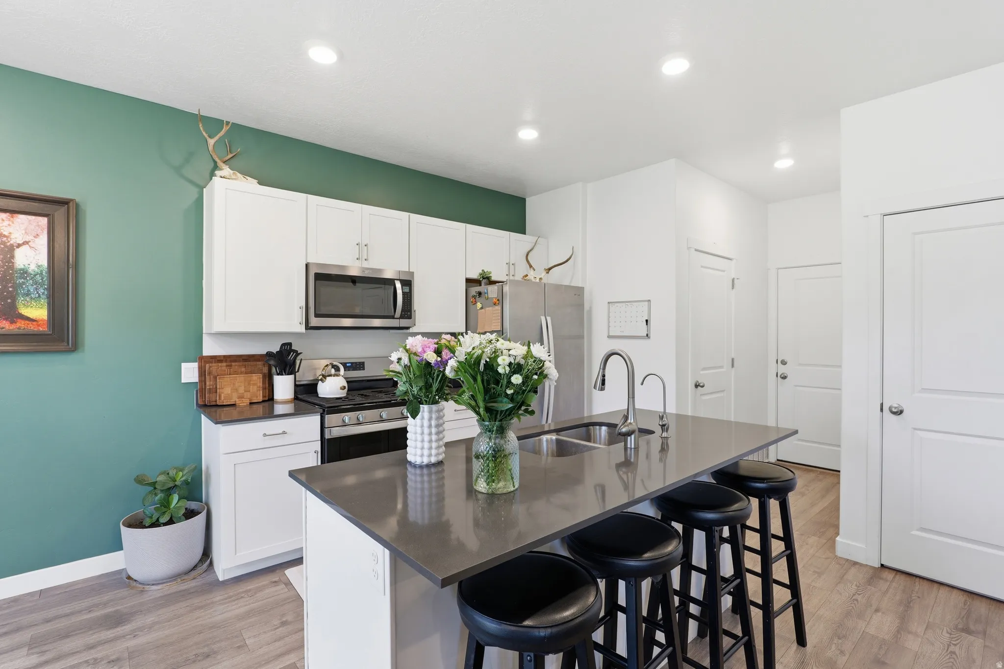 Modern kitchen featuring a central island with a double basin sink, white cabinetry, stainless steel appliances, and wood-finish flooring