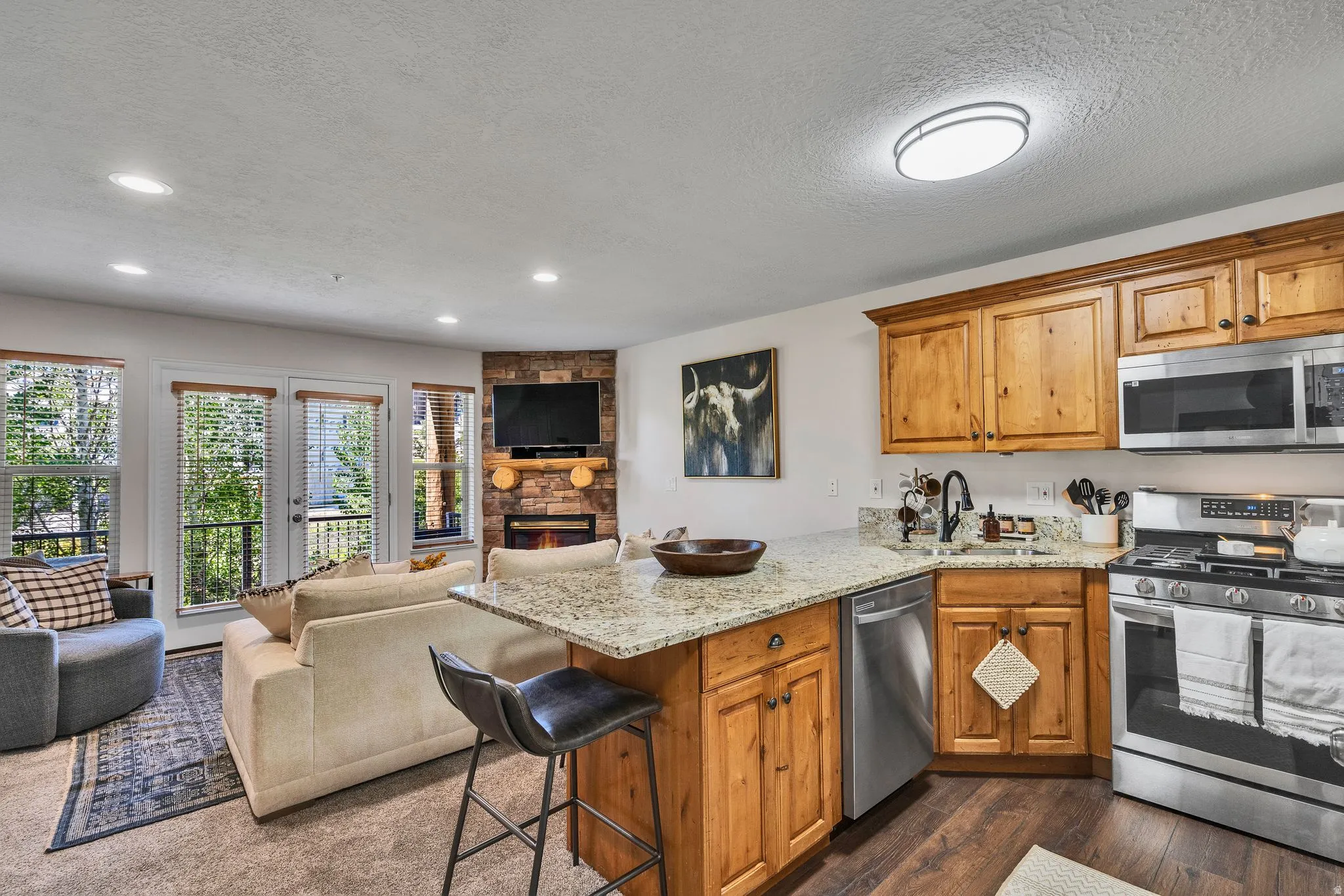 Open-concept kitchen and living area featuring wood-finish flooring, granite countertops, and stainless steel appliances