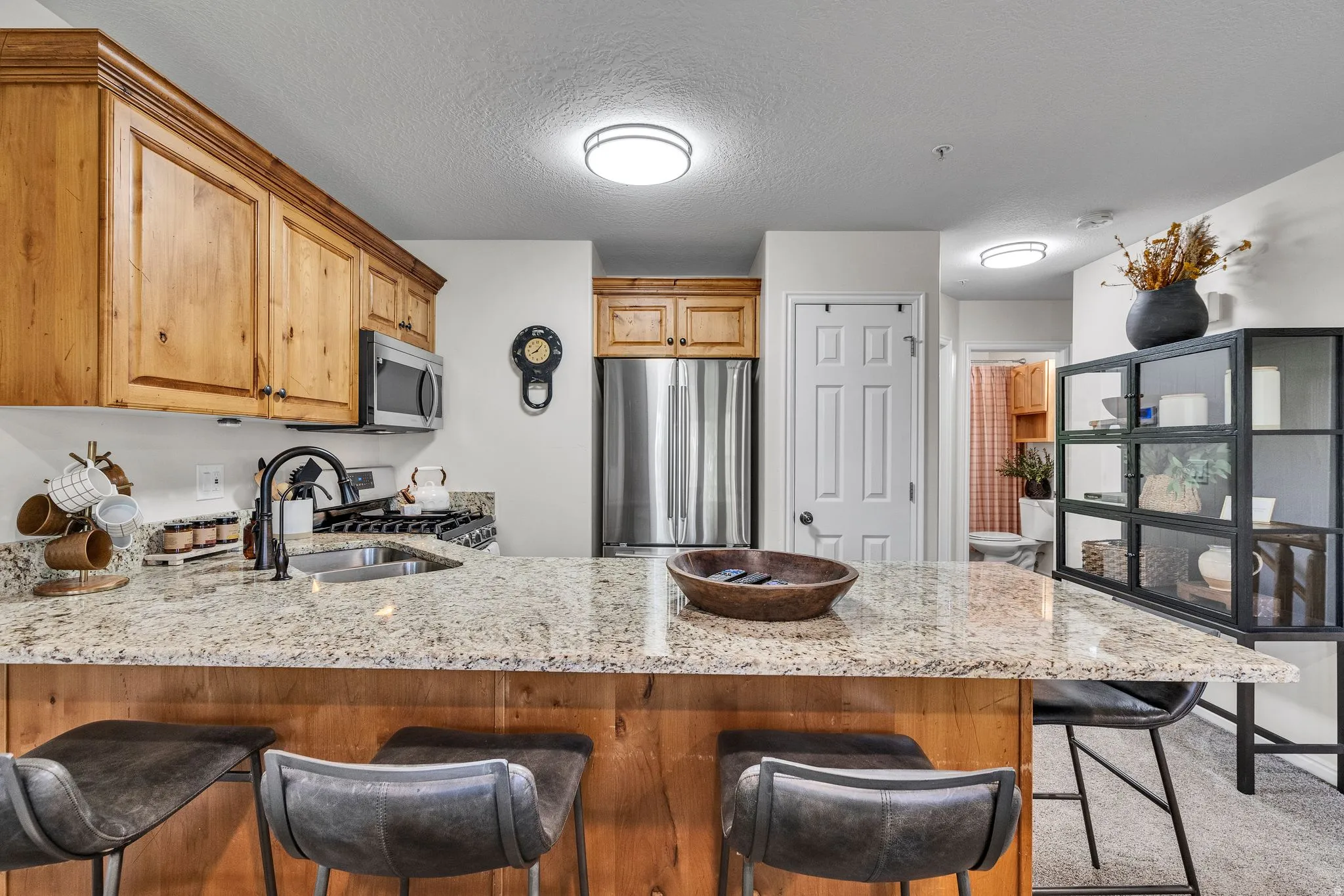 Kitchen featuring a spacious island with granite-finish countertop, wood-finish cabinetry, stainless steel appliances, a gas range, and a matte black faucet