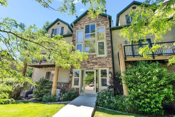 Stone-accented facade with multiple large windows, dormer windows, and two private balconies featuring dark railings