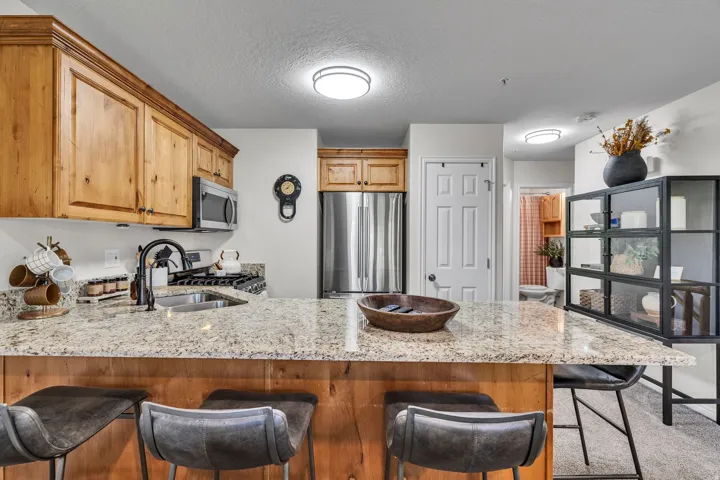 Kitchen featuring a spacious island with granite-finish countertop, wood-finish cabinetry, stainless steel appliances, a gas range, and a matte black faucet