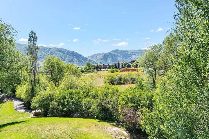 Expansive outdoor grounds featuring a rolling lawn and mature trees, surrounded by distant mountains
