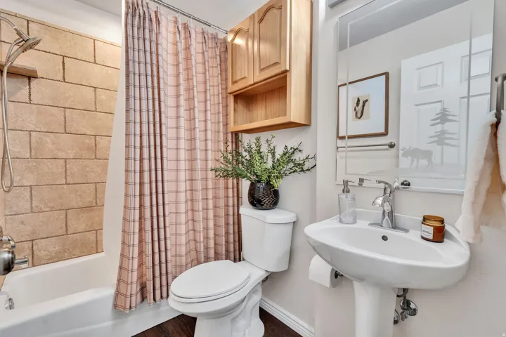 Bathroom with a pedestal sink and chrome faucet, featuring a toilet and an overhead wood cabinet