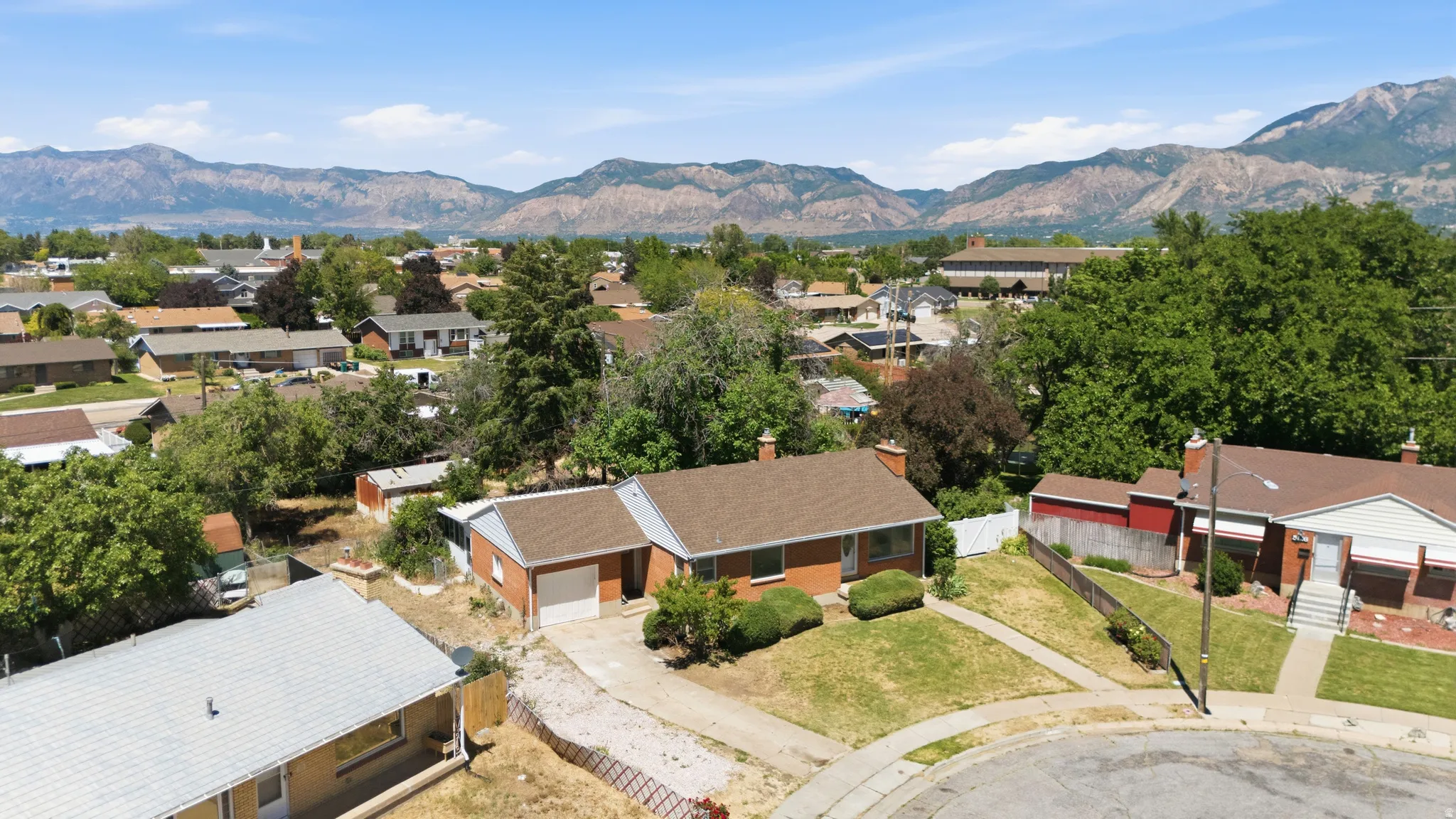 Brick exterior residence with an attached garage, a covered entry, and a front yard with mature landscaping