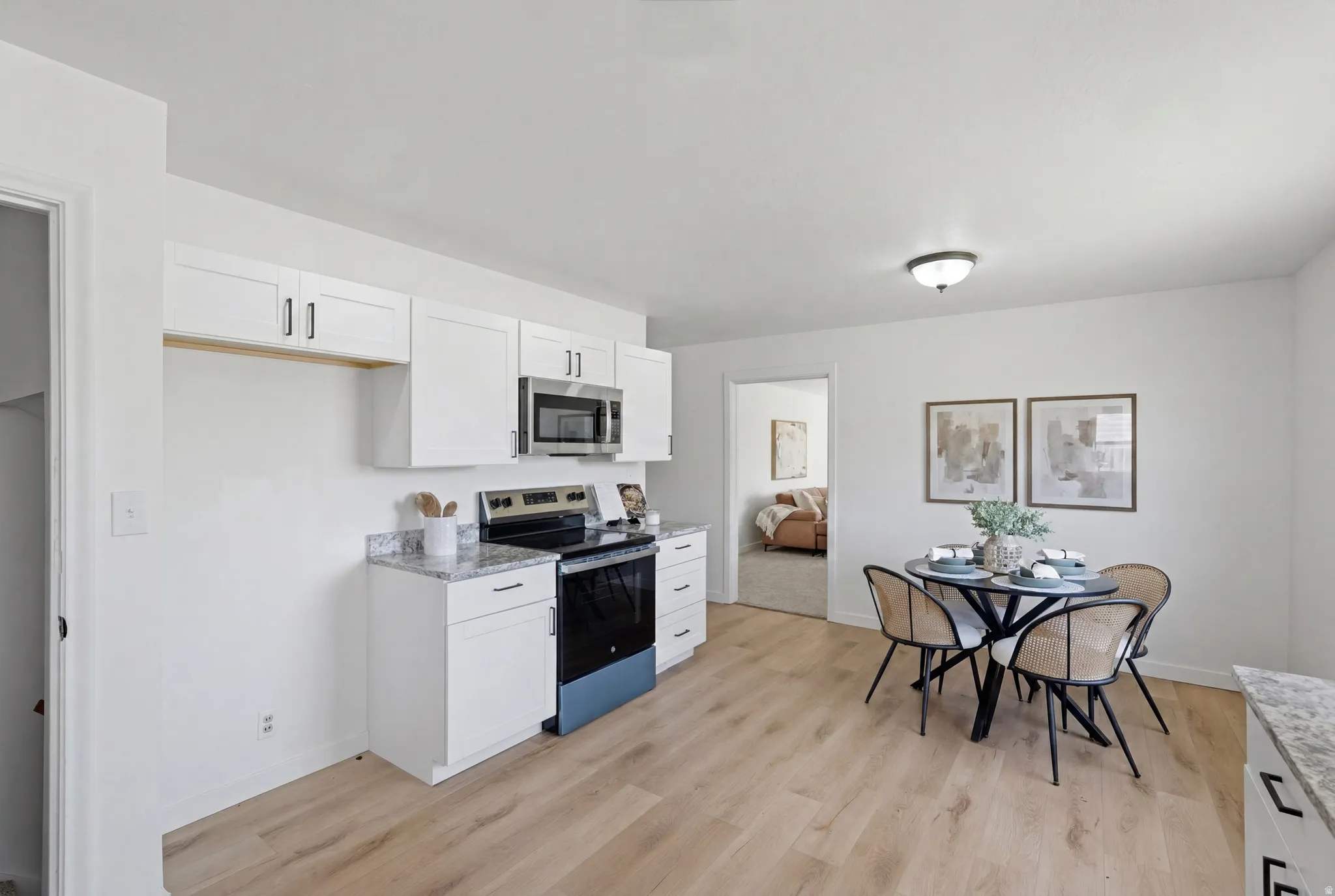 Kitchen and dining area featuring white cabinetry, stainless steel microwave, black range, and light wood-finish flooring