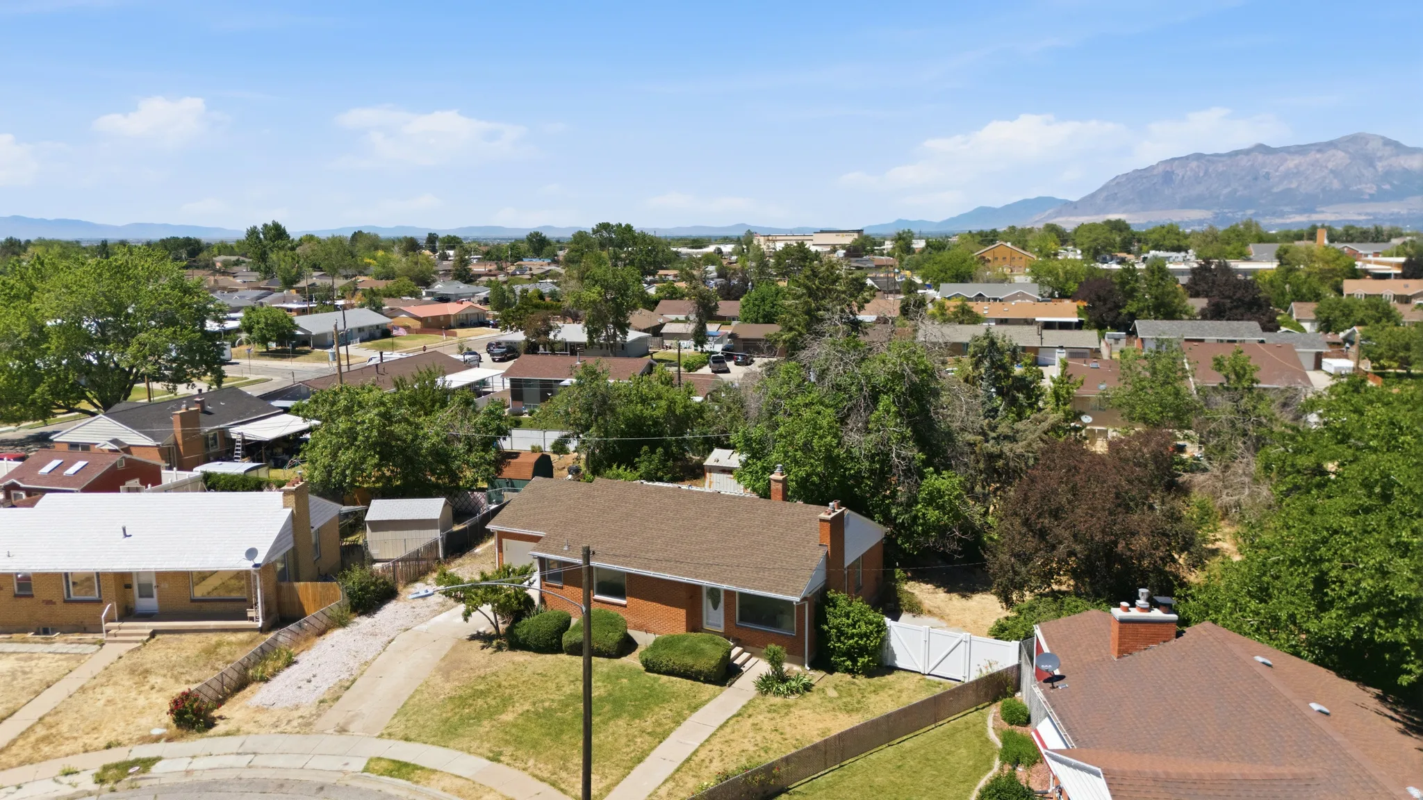Aerial perspective of a neighborhood featuring multiple residential properties with pitched roofs, mature trees, and mountain scenery in the distance