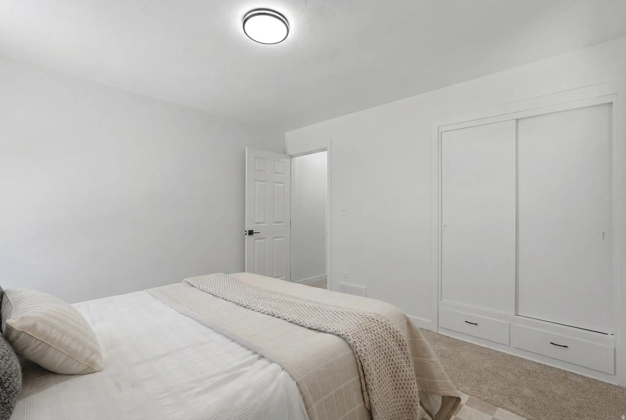 Spacious room featuring neutral carpeting, a modern flush-mount ceiling light, and a built-in closet with sliding doors and integrated lower drawers