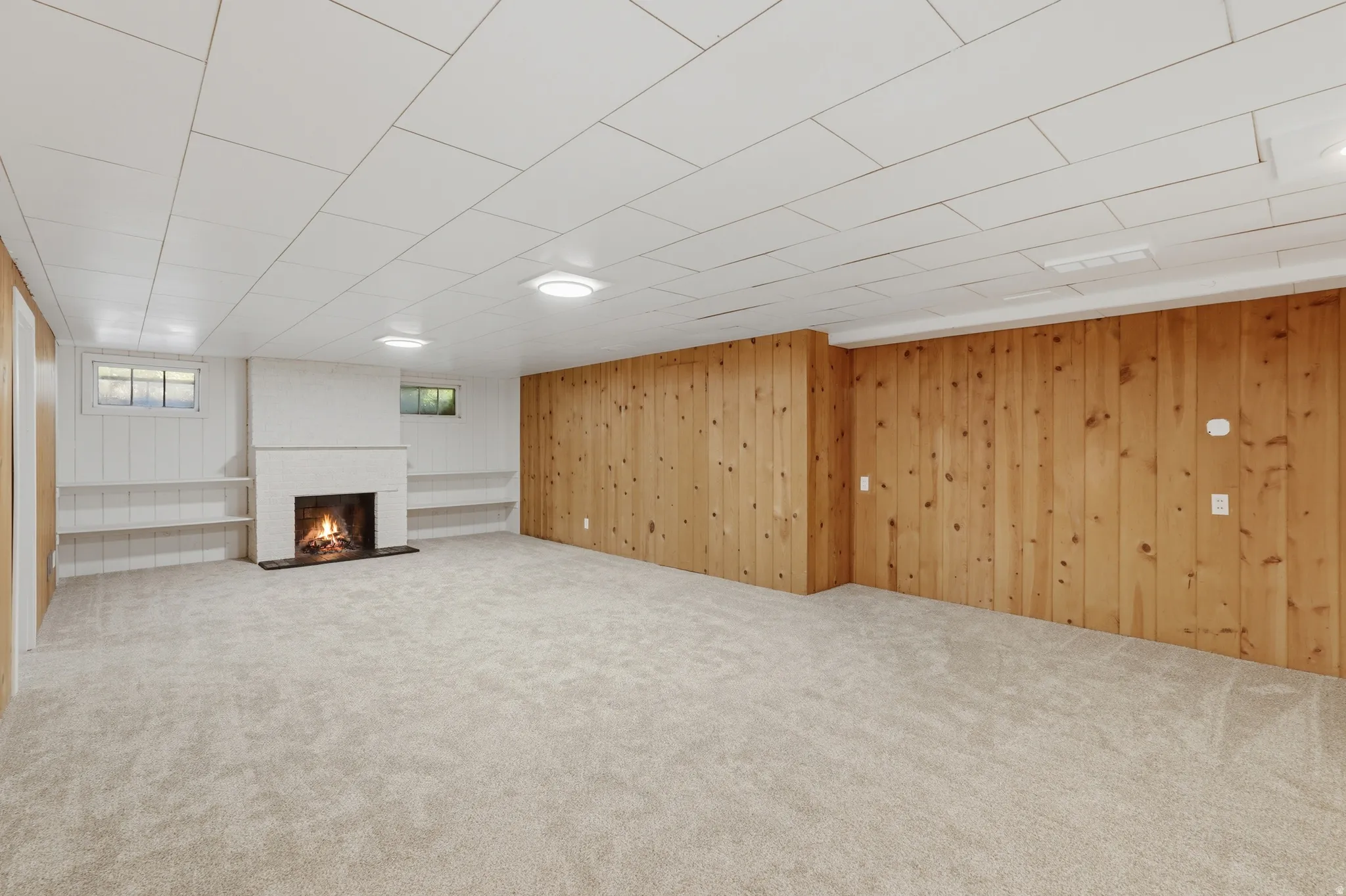 Spacious room featuring a central white fireplace, light-toned carpeting, and wood paneling on one wall