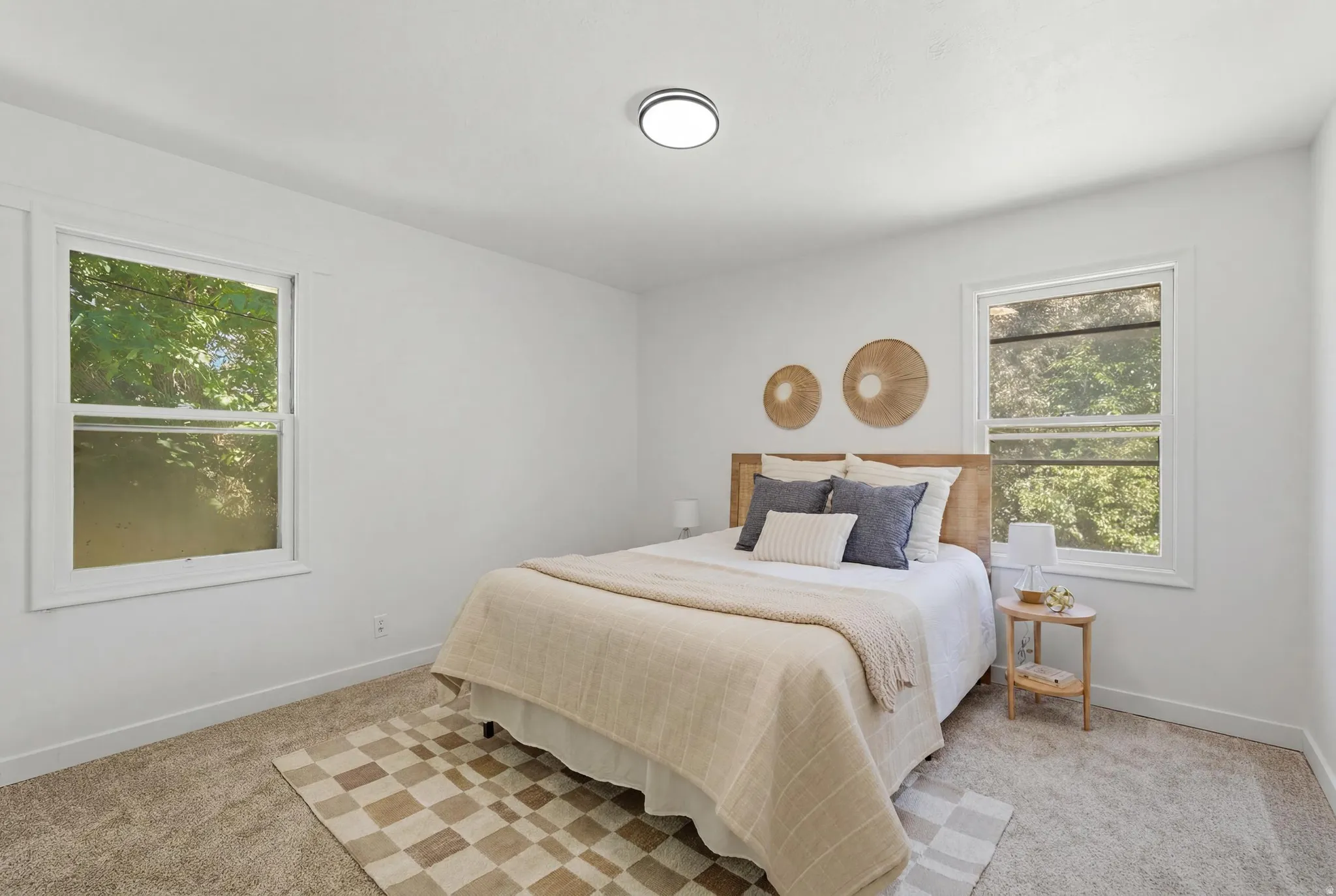 Bright bedroom featuring two large windows, white walls, light-toned carpeting, and a flush-mount ceiling light fixture